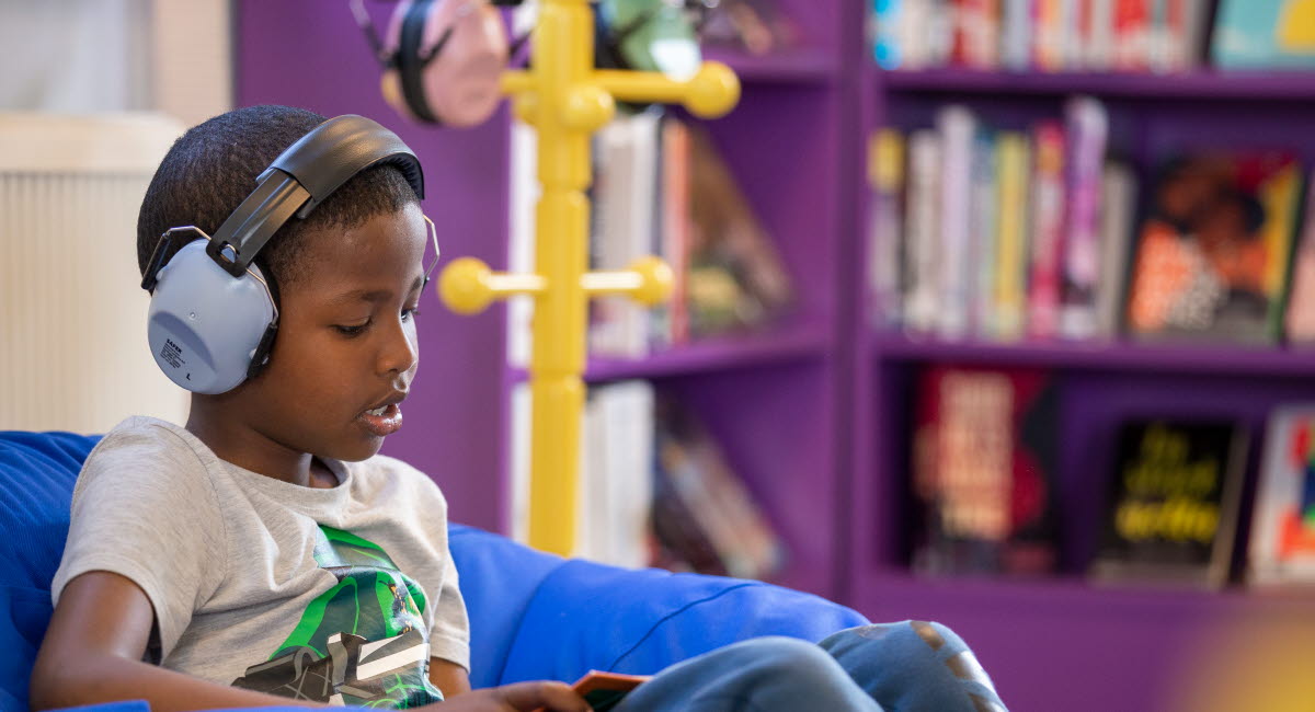 Ett barn sitter med hörlurar i ett bibliotek.
