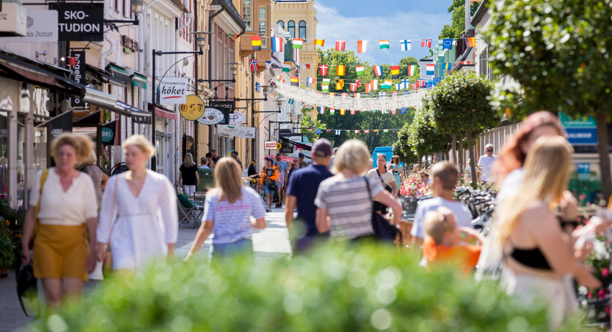 Sommarklädda människor som går runt på en shoppinggata i Västervik på sommaren.
