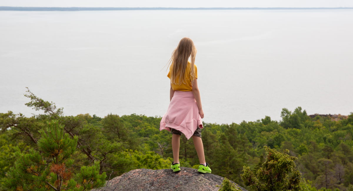 Flicka på en sten som tittar ut över Östersjön