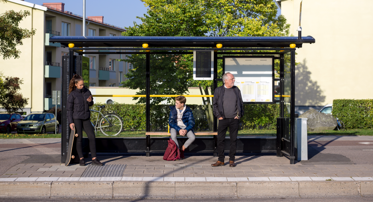 Tre resenärer väntar på bussen vid en hållplats som klassas som B