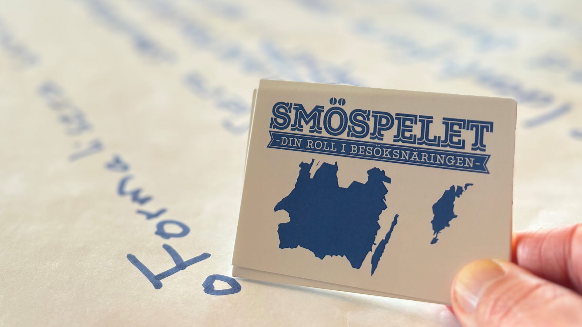 Närbild på spelkort med texten ‘SMÖ-spelet’ och anteckningsblock i bakgrunden.