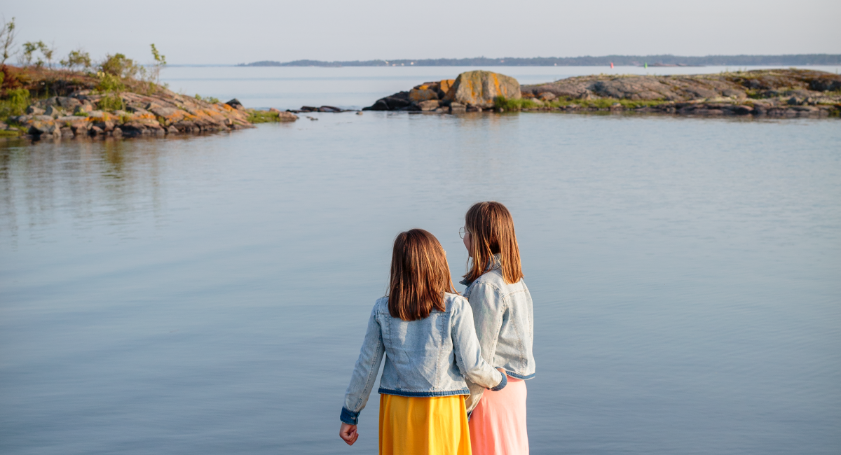 Två flickor står och tittar ut över en sjö.