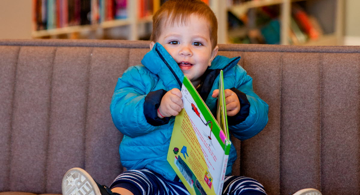 Ett barn sitter i en soffa och läser en bok