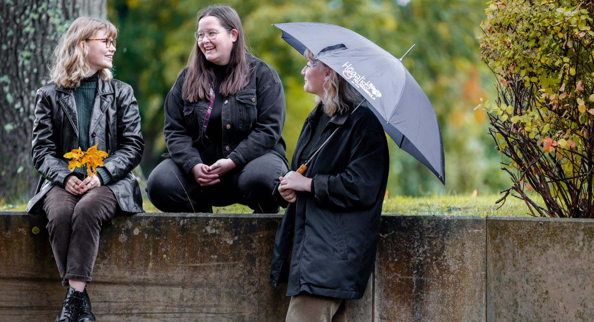 Tre unga kvinnliga deltagare på Högalids folkhögskola pratar vid en trappa.